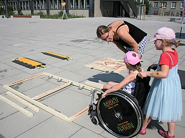Kinder probieren Hindernis-Parcours mit dem Rollstuhl aus, Erwachsene unterstützt