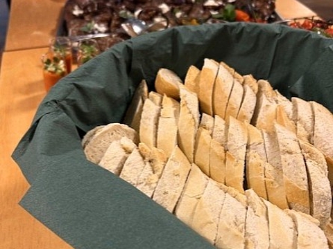 Tisch mit Brotscheiben, Tapas, Aufstrichen und kleinen Gläsern mit Speisen für Gäste einer Ausstellung.