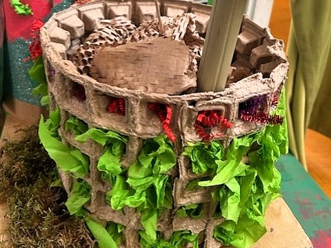 Rundes Modellgebäude aus Karton mit grünen Papierelementen, innen eine Säule mit aufgesetzter Scheibe.