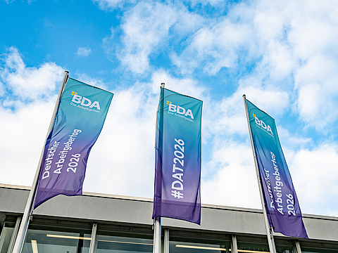 drei Flaggen der BDA vor einem Gebäude, beschriftet mit „Deutscher Arbeitgebertag 2026“ und „#DAT2026“, vor blauem Himmel.