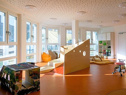 Raum im Kindergarten mit großen Fenstern und Holzelementen zum Spielen