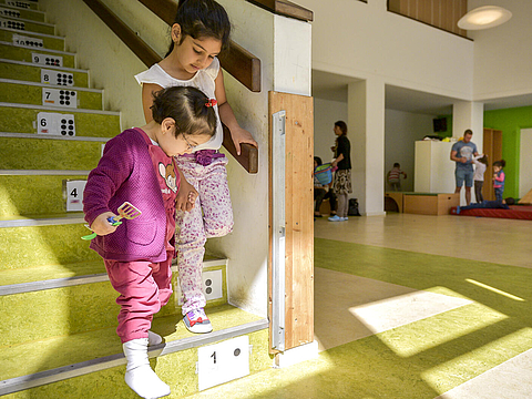 Zwei Kinder steigen gemeinsam eine Treppe in einer Berliner Fröbel-Kita hinunter - die Treppenstufen sind nummeriert, mit Ziffern und Punkten. Auch das ist alltagsintegrierte mathematische Bildung. (Foto: Fröbel e.V./Bettina Straub)