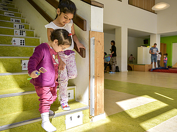 Zwei Kinder steigen gemeinsam eine Treppe in einer Berliner Fröbel-Kita hinunter - die Treppenstufen sind nummeriert, mit Ziffern und Punkten. Auch das ist alltagsintegrierte mathematische Bildung. (Foto: Fröbel e.V./Bettina Straub)