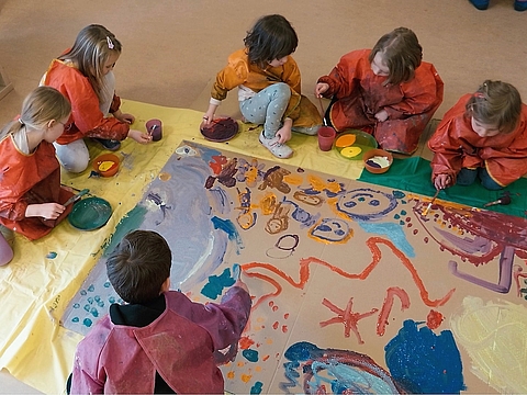 Kinder gestalten im Kita-Atelier das Bühnenbild mit Pappe, Pinseln und Farbe.