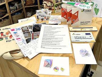 Materialien für den internationalen Austausch liegen auf einem Tisch: Kinderzeichnungen, Bücher, Briefe und Informationsmaterialien.