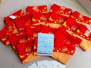 Mehrere rote Badetücher liegen halbkreisförmig auf dem Boden. In der Mitte liegt ein Flyer mit Baderegeln für Kinder.