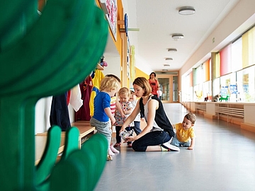 Foto einer Erzieherin mit Kindern in der Garderobe der Kinderkrippe