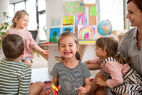 Lächelndes Kind im Vordergrund, Gruppe von Kindern und erwachsene Person im Hintergrund
