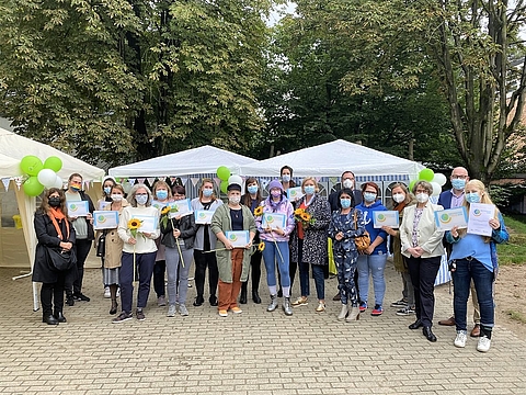 Gruppenfoto mit mehreren Erwachsenen, die Urkunden und Blumen in den Händen halten.