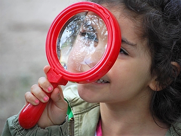 Foto von einem Kind, das durch eine große Lupe schaut und lächelt