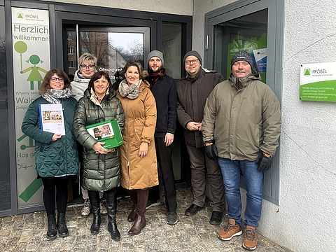 Eine Gruppe von Personen steht vor der Fröbel-Geschäftsstelle in Frankfurt an der Oder. Sie tragen winterliche Kleidung und lächeln in die Kamera.