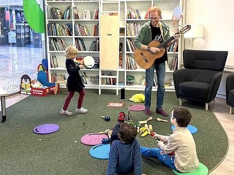 Henning Petersen spielt die Gitarre, Kinder mit Instrumenten begleiten ihn